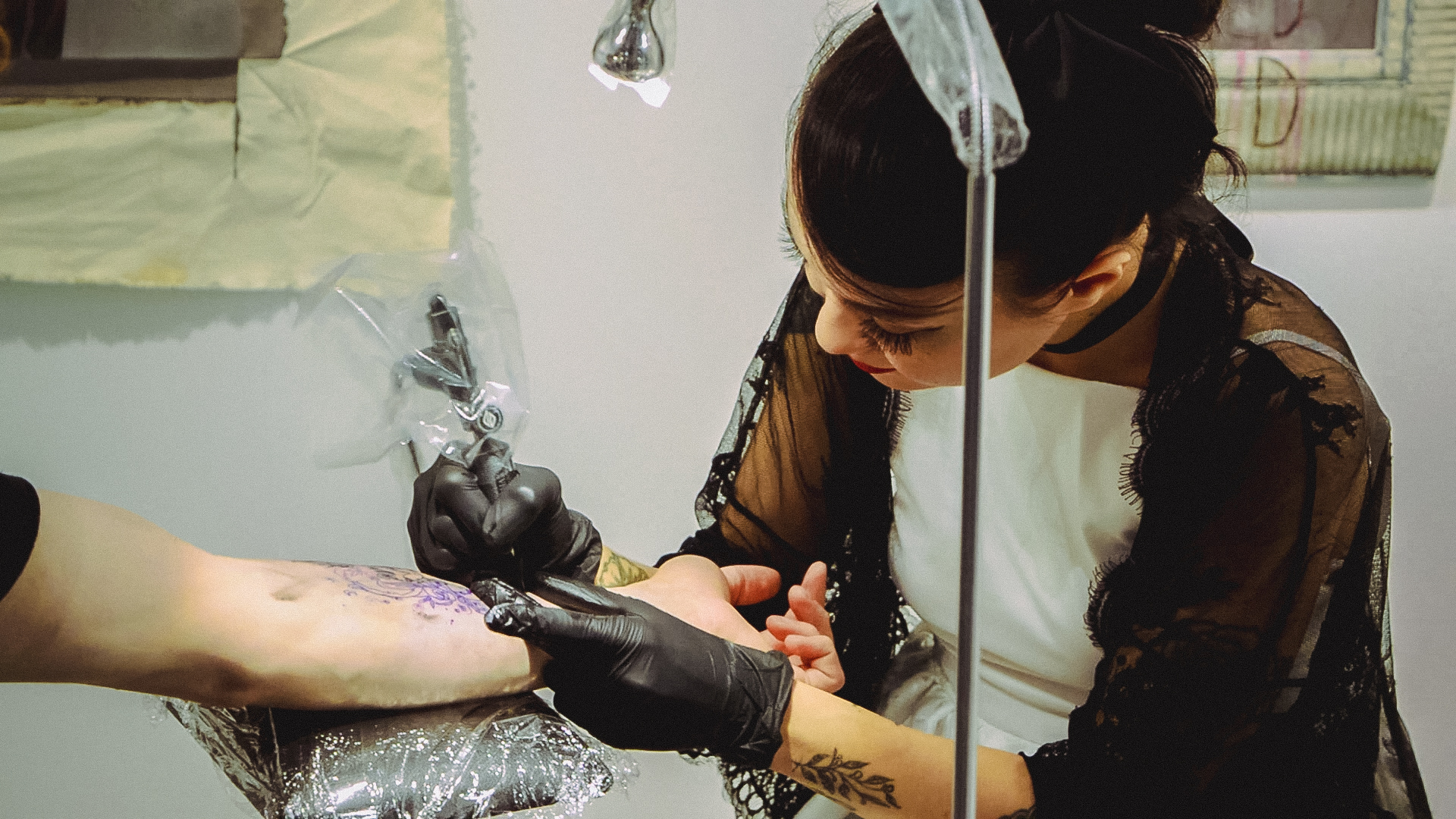 A tattoo artist working with a visitor beside displayed artwork